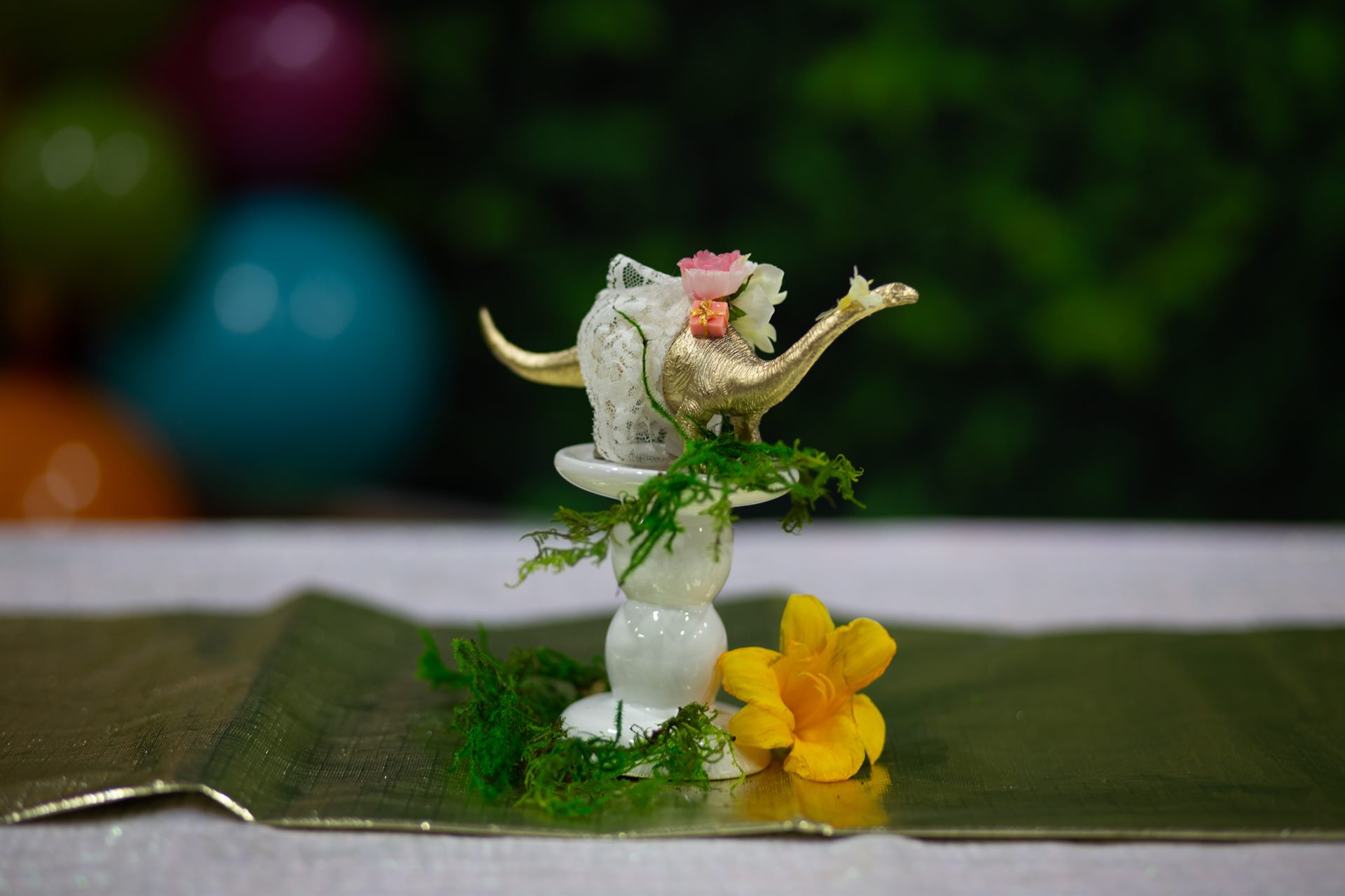 Close-up of a gold dinosaur centerpiece with lace, blossoms and moss