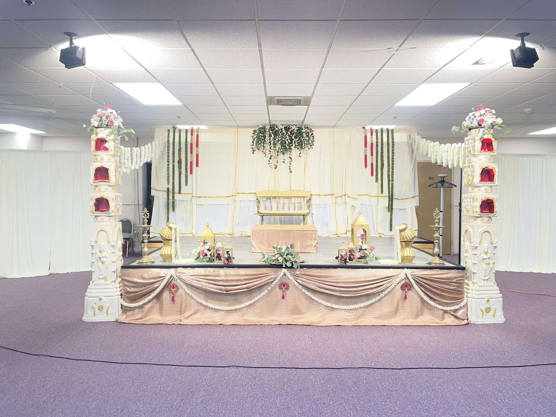 Traditional mandap stage with pillars, garlands, and brass lamps