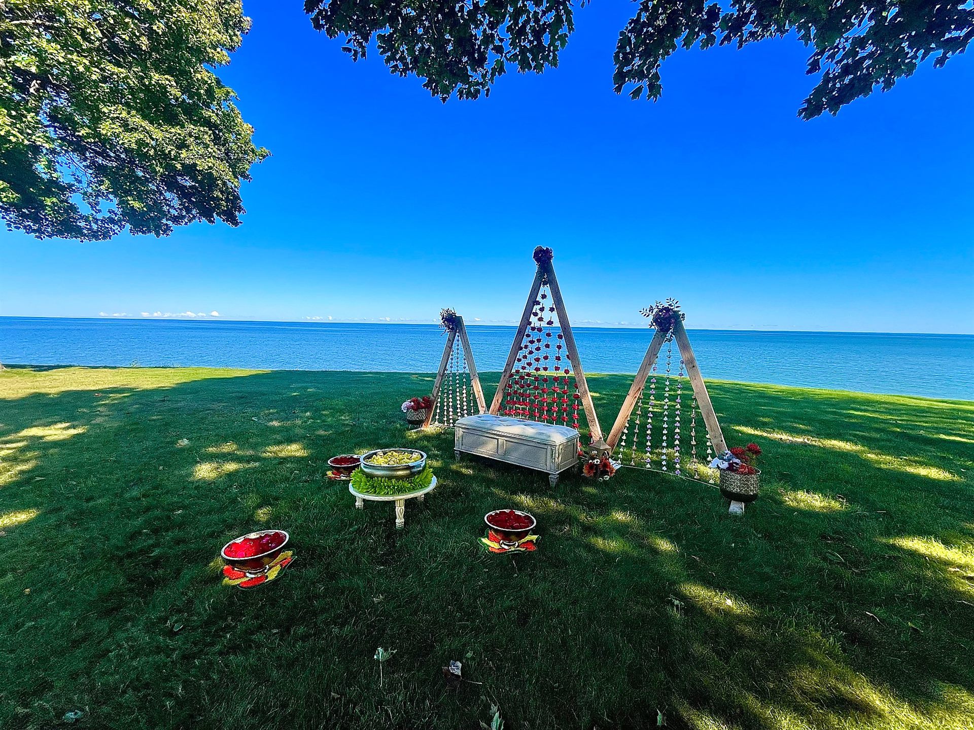 Three flower-strung wooden frames and ceremonial arrangements on a lakeside lawn