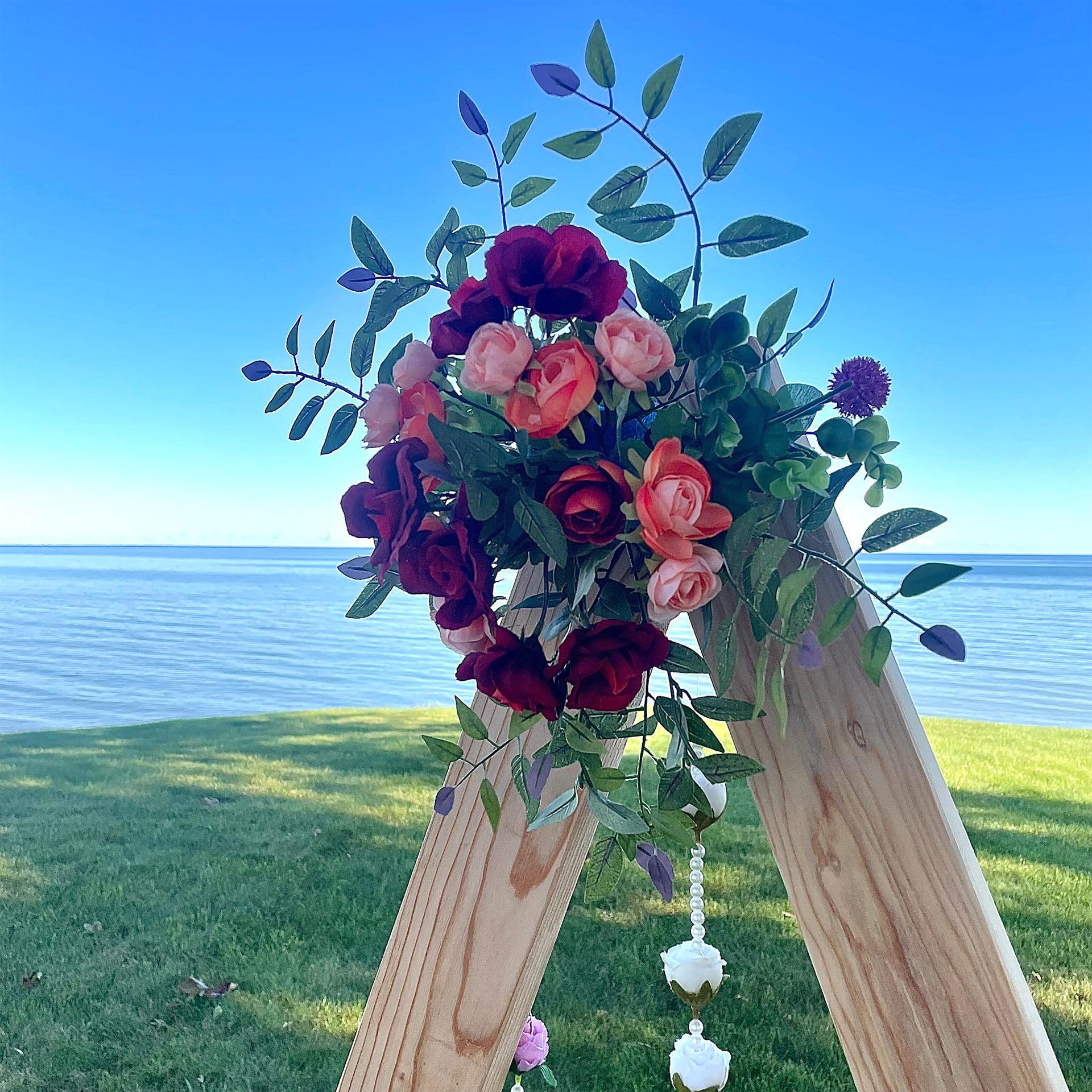 Burgundy and blush floral arrangement on a wooden ceremony frame beside the water