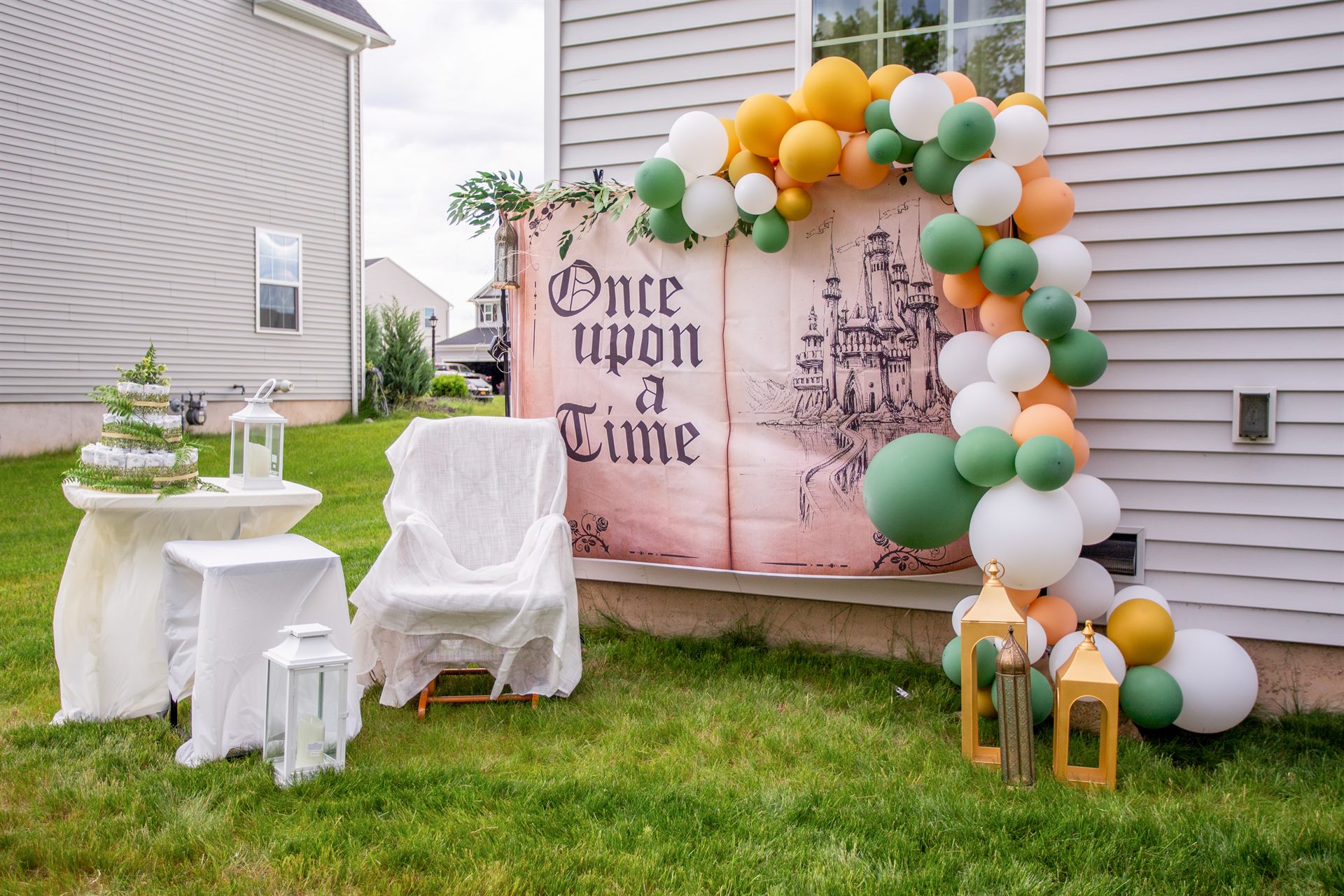 Once Upon a Time storybook baby shower backdrop with sage, peach and gold balloon arch, gold lanterns and diaper cake