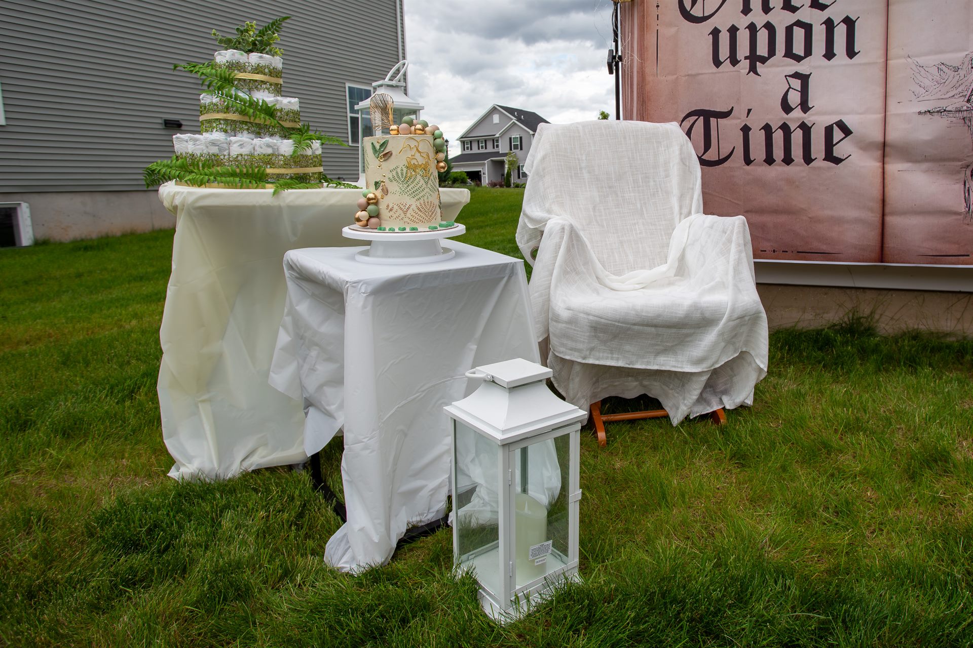 Greenery and gold baby shower cake beside a fern-trimmed diaper tower on draped tables